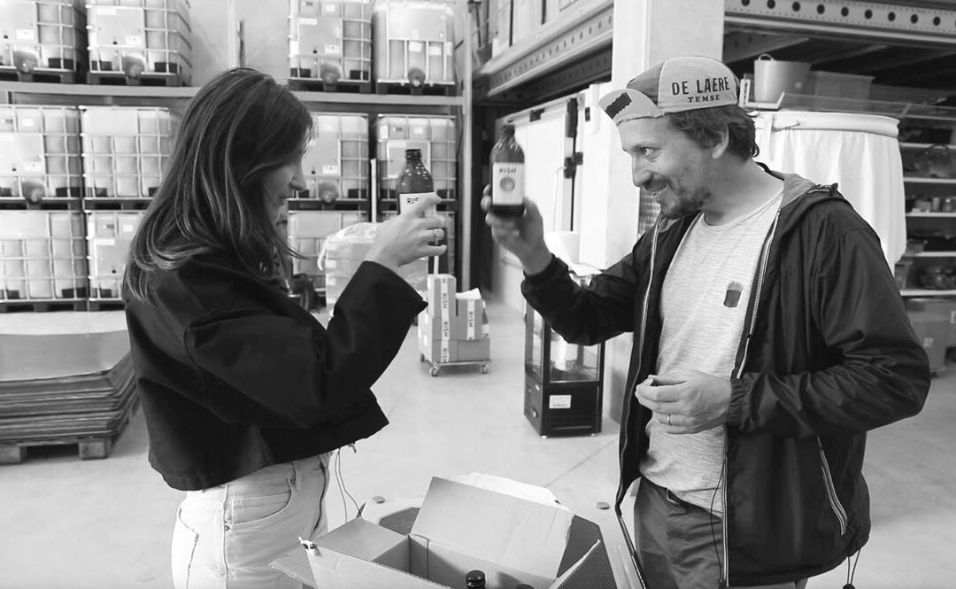 Julien Dewitte et une invitée trinquent avec des bouteilles dans un entrepôt